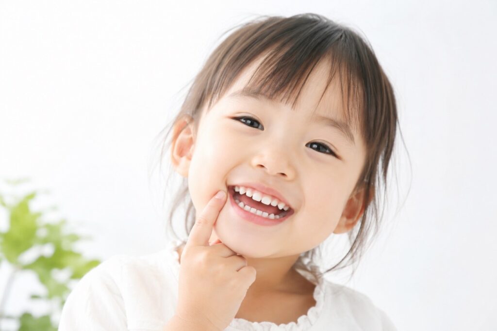 子どもの女の子が笑顔で自分の歯を指さしている画像